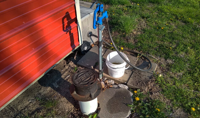 white bucket at base of water pump with grey hose